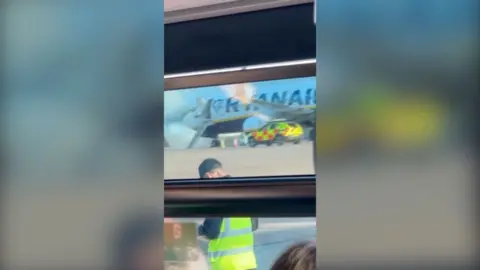 An exterior view of a Ryanair plane with smoke coming out the front