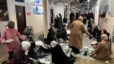 Shariqua Ahmed/BBC Women sitting on green mats, sharing a meal inside the stadiums corridor.
