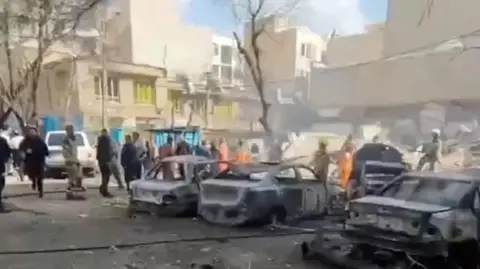People gather near burnt vehicles in Tehran after earlier strikes