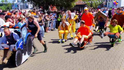 JAS Photo Five different pairs of men take part in the Watchet Wheelbarrow Race, watched on by hundreds of people. One pair is dressed as characters from Scooby Doo, while another wear suits made to look like beer. 