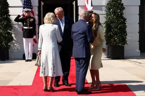 Reuters The royal couple, in formal dress, greet Donald and Melania Trump on a red carpet. In the background two soldiers salute in front of UK and US flags