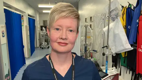 A woman with short blonde hair and blue scrubs 