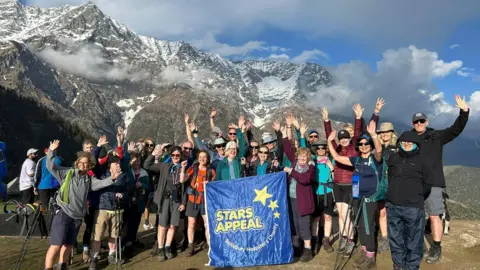 Salisbury District Hospital's Charity A group of people cheer and wave their arms in front of a mountain