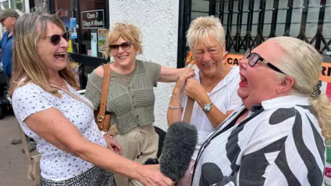 Sue and customer laugh with Claire outside her shop 