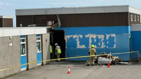 Firefighters behind a yellow cordon investigate the damage to Dales Park primary school