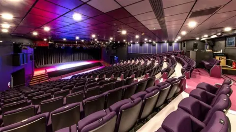 States of Guernsey An empty theatre. The seats are covered in maroon upholstery.