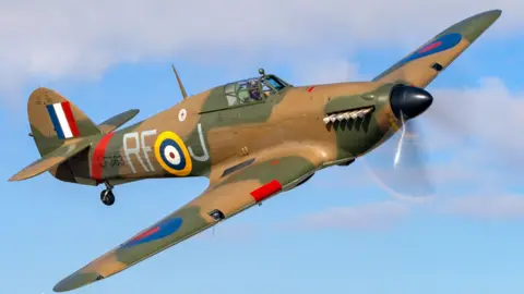 Darren Harbar/Crown Copyright BBMF Hurricane LF363 flying through the air against a blue sky. The aeroplane is painted in camouflage colours with RF on its side. There is one pilot in its cockpit. 