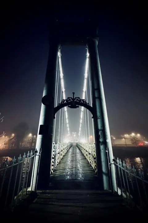 James McLeod A set of lights strung across a bridge on a misty morning while the sky is still dark