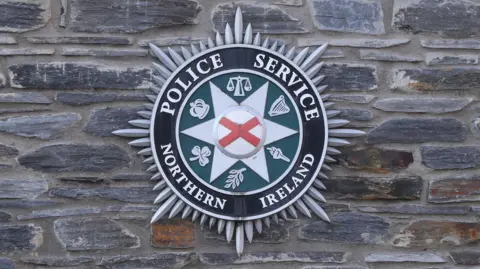 PSNI crest that says Police Service of Northern Ireland - on a stone wall. 
