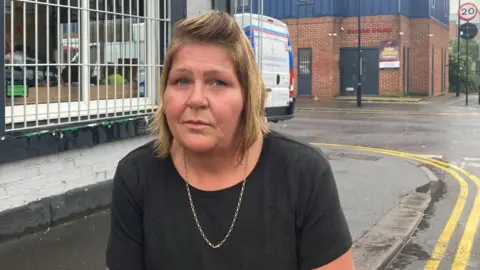 Simon Thake/BBC A woman stands in front of a cafe next to double yellow lines