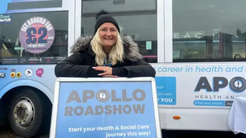 Andrew Turner/BBC Debbie Sampson standing and leaning on an advertising board for the Apollo Roadshow