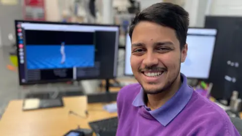 Nathan is smiling and wearing a purple sweatshirt