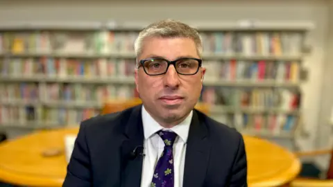 Mark Arnull, a man in glasses and a navy blazer and white shirt and purple tie, seated in a library.
