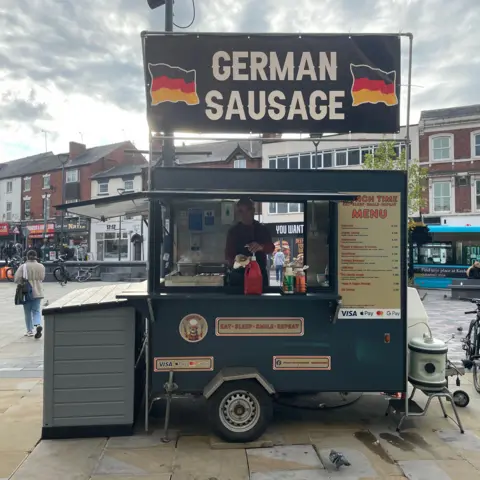 Sausage Man serving a hotdog in his new sausage stall