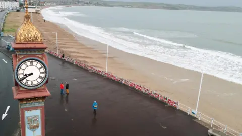 Dorset Council Weymouth's Jubilee Clock with the esplanade running alongside and hundreds of festival stockings attached to the seafront railings.