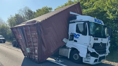 TVP Roads Policing A shipping container collapsed on the back of a truck, one side in the road. The cab is also smashed.