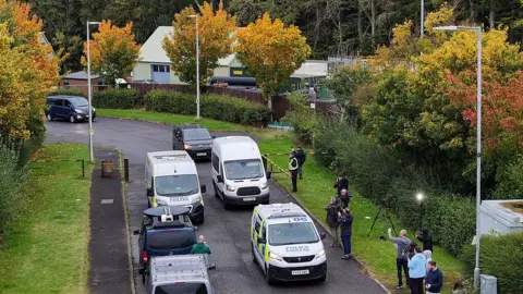 Getty Images A drone shot of two police vans and several other unmarked vans on a road. Cameras and journalists are filming them. 