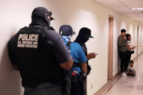 Getty Images People wait to enter immigration court as federal agents patrol the halls 