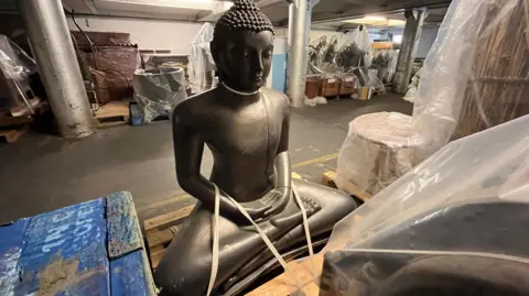 The model of a deity with crossed legs in pictured on a wooden shelf in the museum's store.