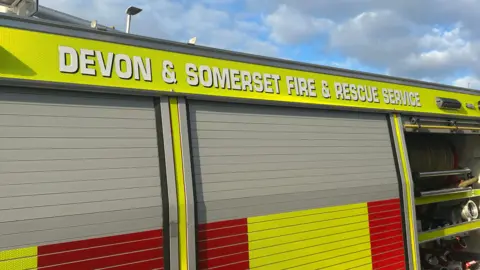 A picture of the side of a Devon and Somerset fire vehicle. It is red and green in colour with the force name at the top of the vehicle.