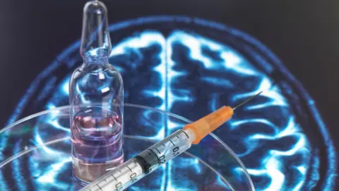 Getty Images Glass vial and injection needle sitting on an image of someone's brain