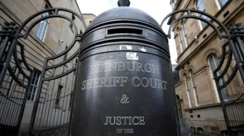 Large sign in front of metal gate bars and sandstone walls that says Edinburgh Sheriff Court