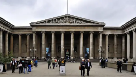Groups of people stand outside the entrance of the British Museum in London.
