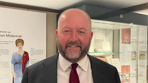Vikki Irwin/BBC A head and shoulders image of Nick Timothy. He is wearing a suit and a white shirt with a red tie. He is smiling and looking into the camera.