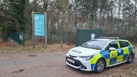 Henry Godfrey-Evans/BBC A police car parked at the entrance of a reservoir. There is a large green gate and fence marking the boundary of the site. There is also a large blue sign detailing the name of the reservoir.