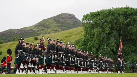 PA Media Lines of soldiers and military personnel wearing uniforms in the gardens on the Palace of Holyroodhouse. Arthur Seat is in the background.