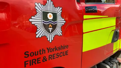 A close-up of the side of a red fire engine. It has the words South Yorkshire Fire & Rescue written on it beneath the brigade's crest.