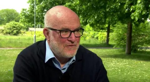 Picture of University of Reading food security expert Richard Tiffin sitting outside on a bench at the University with small trees and grass in the background.