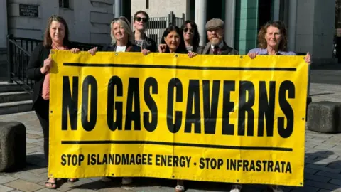 BBC Campaigners standing outside Belfast Laganside Court holding a banner reading "No gas caverns" 