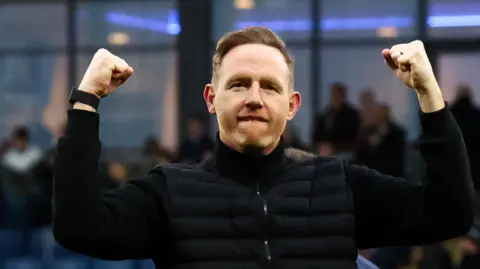 Shrewsbury Town head coach Gavin Cowan holds both fists up in the air in celebration