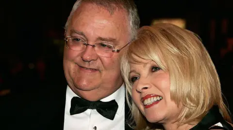 Getty Images Ian Smith with wife Gail, who died in 2019. He is wearing a black tuxedo, she has her blonde hair down and  you can just see the top of her black collar.