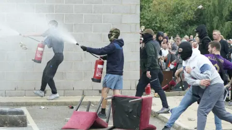 PA Media A protester uses a fire extinguisher on police officers as trouble flares during an anti-immigration protest outside the Holiday Inn Express in Rotherham. 