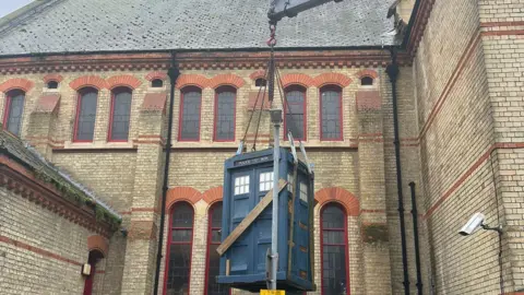 Zion Baptist Church Tardis is being lifted in to the courtyard. In the background, the church building can be seen and the top of the crane. 
