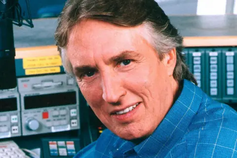 Johnnie Walker wearing a blue shirt with radio equipment in the background.