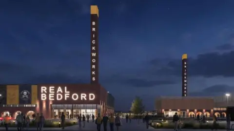 An artist's impression of a sporting campus including a football stadium belonging to Real Bedford. There are two tall chimney like structures with the word "Brickworks" down the side. It is a night time scene and people are walking around with the lights on in the background.