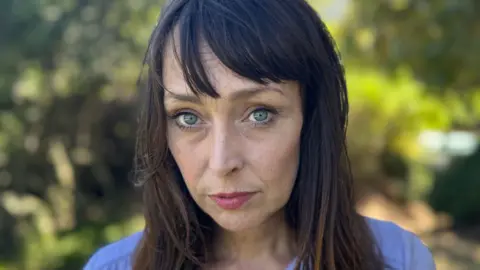 Juliette Bryant, now aged 43, has long brown hair with a fringe and stands outside with a serious expression 
