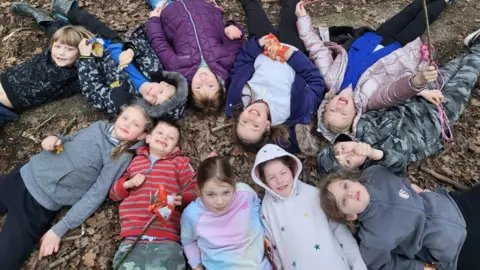 A group of children lying on the floor in a forest at a Romsey Young Carers activity day