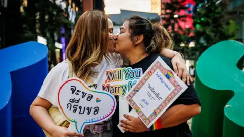 Getty Images Chumaporn "Waaddao" Taengkliang və onun sevgilisi Nongnapat Jonjaroen, 25 sentyabr 2024-cü ildə Banqkokda Taylandın nikah bərabərliyi qanun layihəsini qeyd edərkən öpüşürlər.