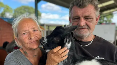 Elliot Deady/BBC Sandy Miller and Gary Clarke with a goat at their farm in St Osyth