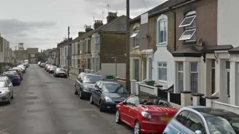 A street with terraced houses and cars on it.
