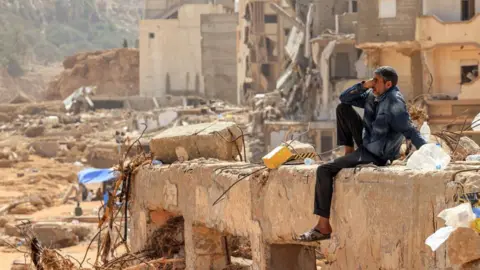 Getty Images Een man reageert terwijl hij op 18 september 2023 op het puin van een verwoest gebouw in de Oost-Libische stad Derna zit na dodelijke overstromingen