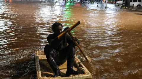EPA A Kenyan man is seen crossing flooded road using a makeshift raft during heavy rain in Nairobi