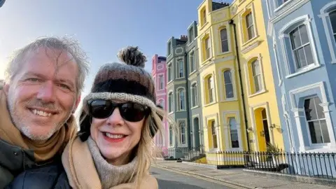 Jeff and his wife fran smiling at the camera stood in front of colourful houses