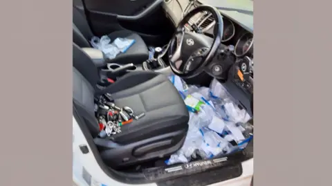 Avon and Somerset Police A car is seen with the passenger door open and on the seat are various keys to other vehicles while dozens of plastic bags are visible on the floor