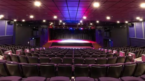 States of Guernsey An empty theatre. The seats are covered in maroon upholstery.