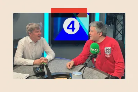 Nick Watt wears a light shirt as he sits in a studio to speak with Sunder Katwala, who is wearing a red 1966 replica England football jersey